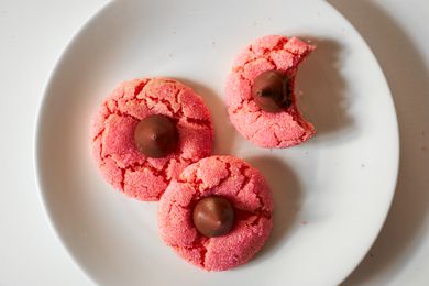 Overhead view of a white plate of three strawberry chocolate kiss cookies on a white background