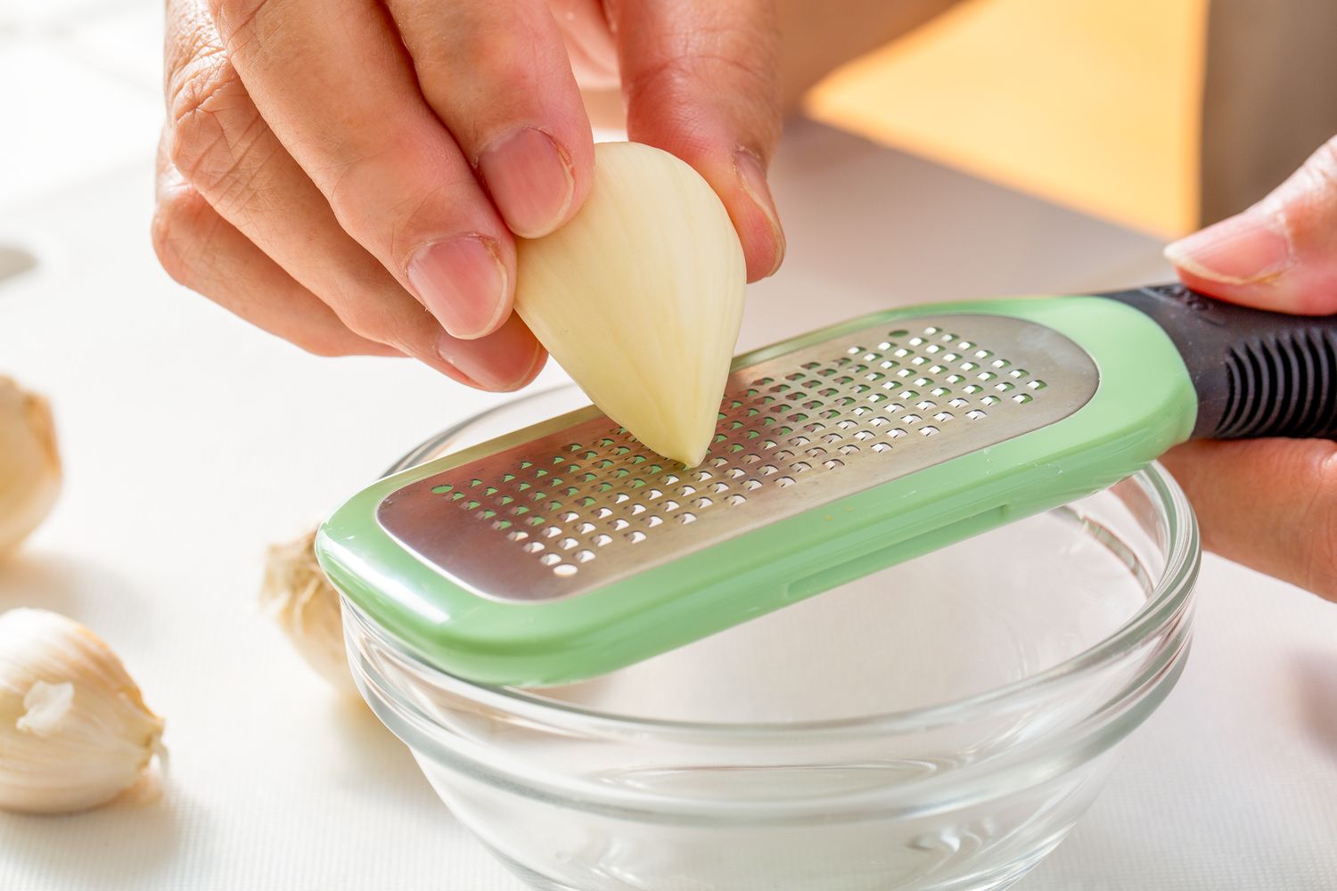 Hand grating a clove of garlic over a small bowl using a microplane grater