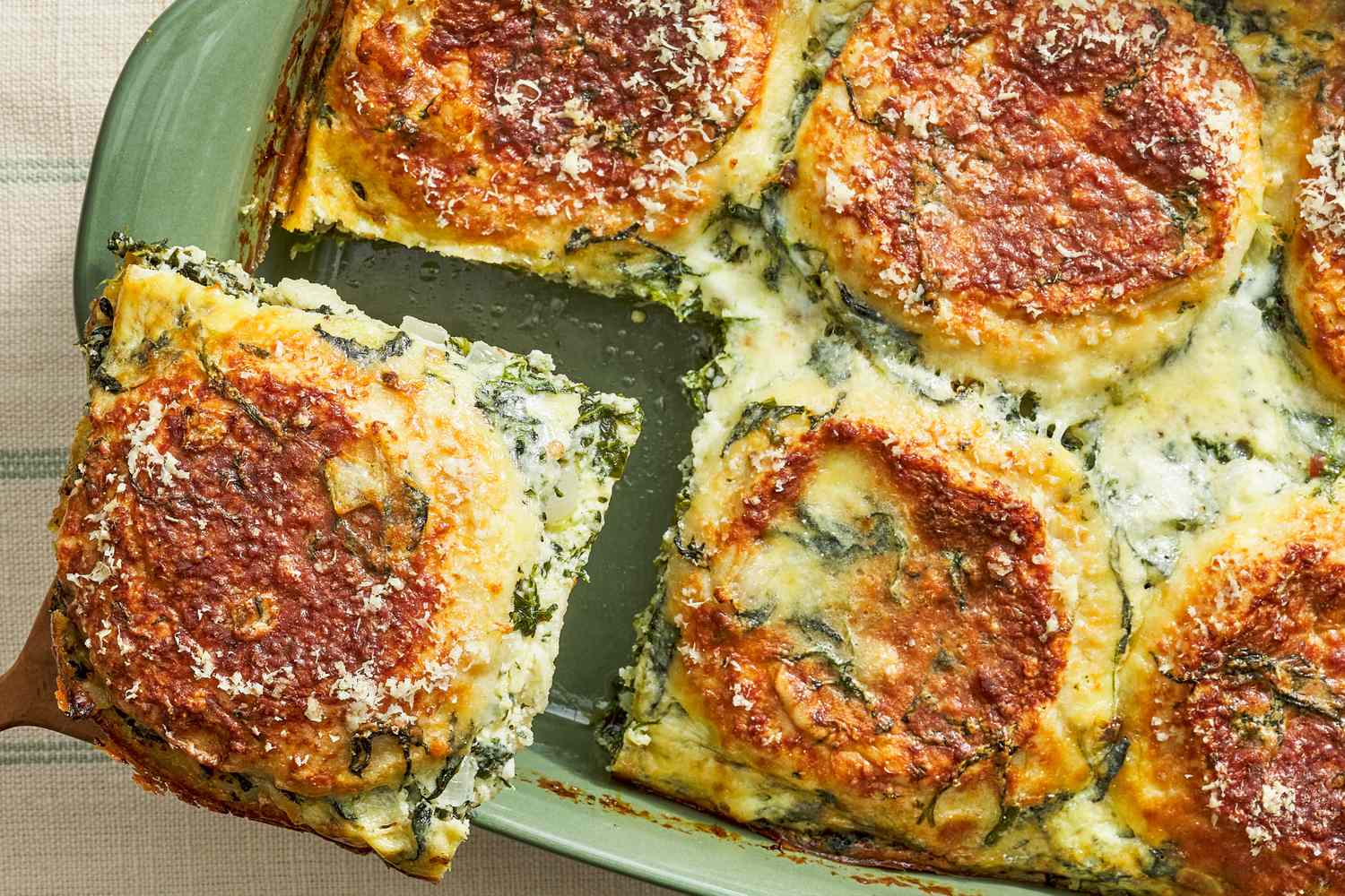 A baked spinach and cheese lasagna being served from a casserole dish