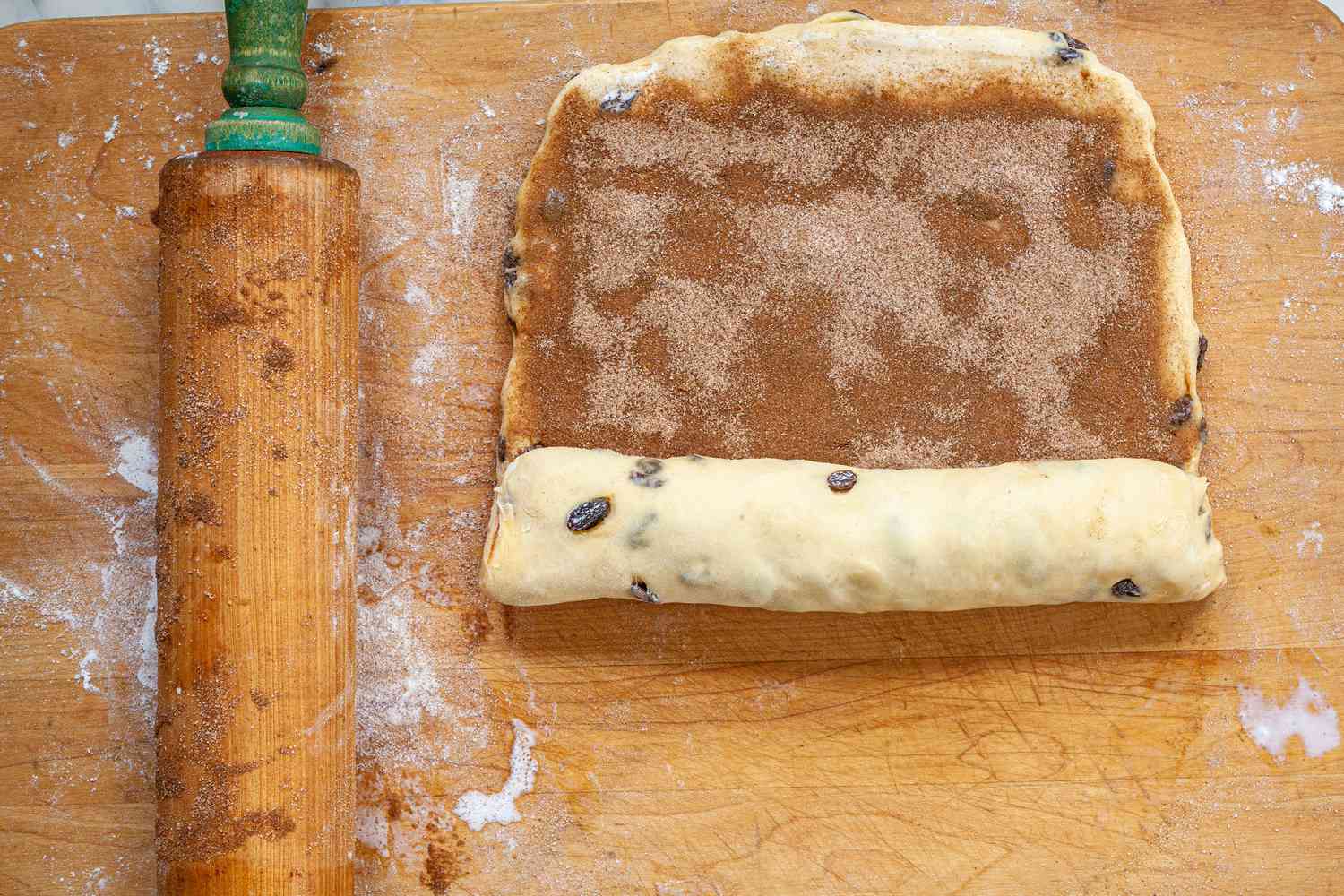Cinnamon Sugar Mixture Added to Cinnamon Swirl Raisin Brioche Rectangle and Rolled on a Cutting Board