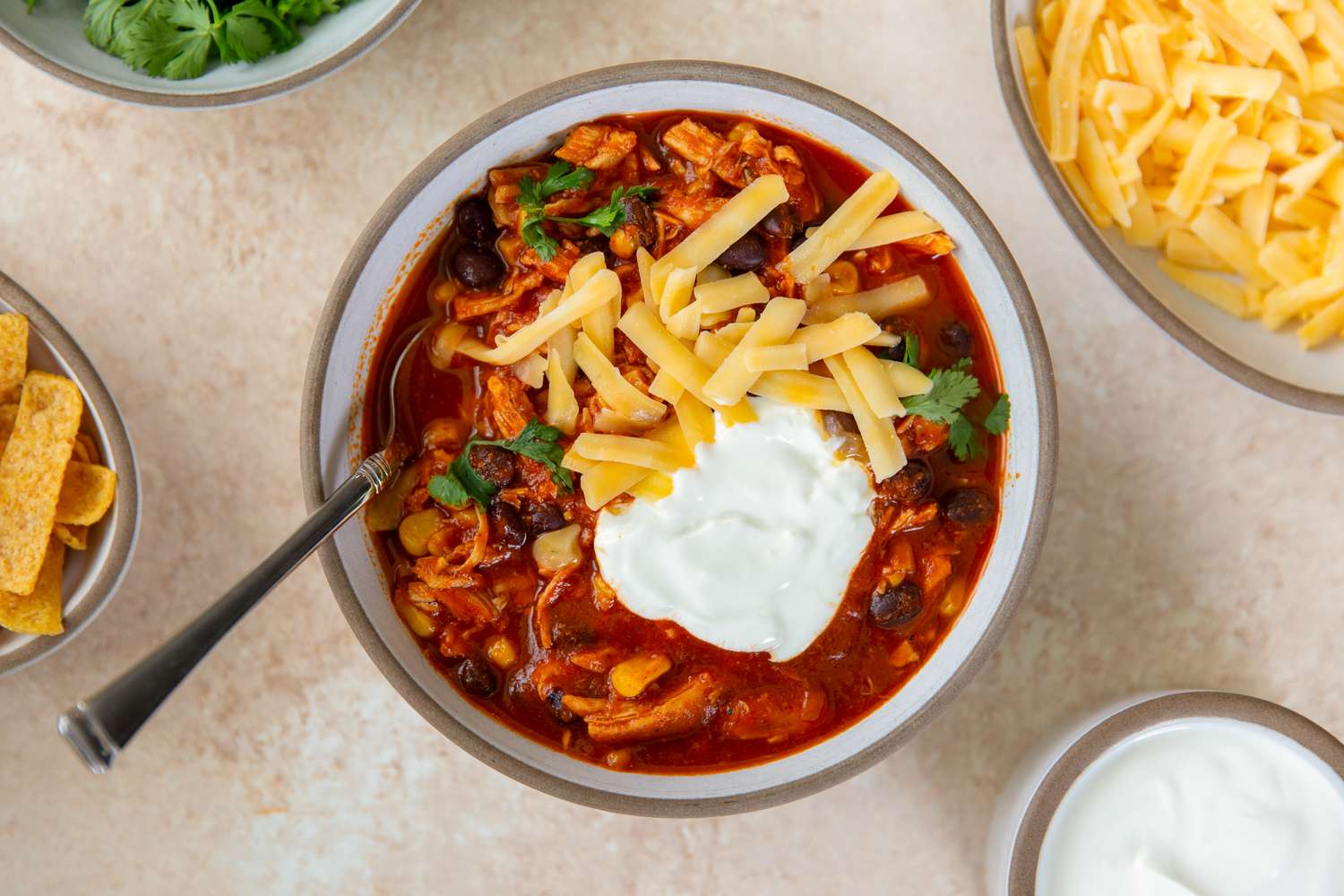 A bowl of chicken enchilada chili topped with shredded cheese sour cream and cilantro