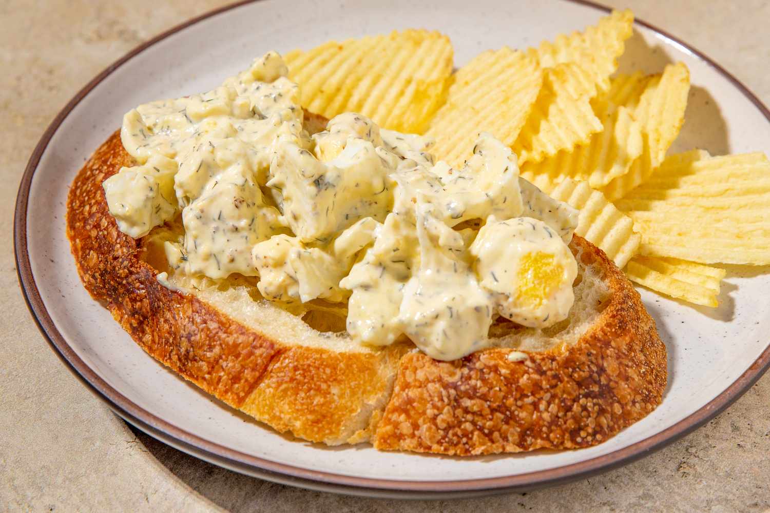 Egg salad on a slice of bread alongside ridged potato chips