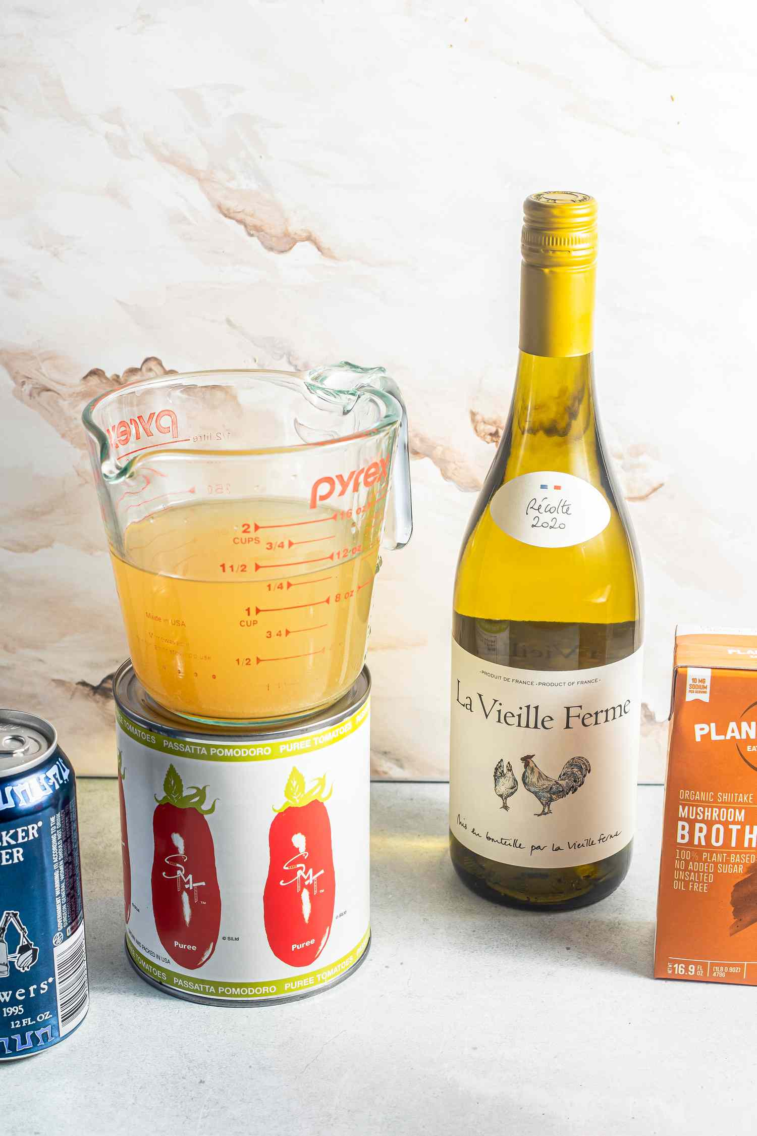 Items to Use to Deglaze a Pan (L to R): Can of Beer, Can of Tomato Puree, Pyrex Measuring Cup of Stock, Bottle of White Wine, Glass of Red Wine, and a Box of Mushroom Broth for How to Deglaze a Pan