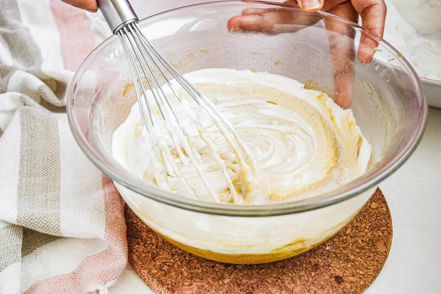 Whisking custard into whipped cream in a large glass bowl to make a custard dessert.