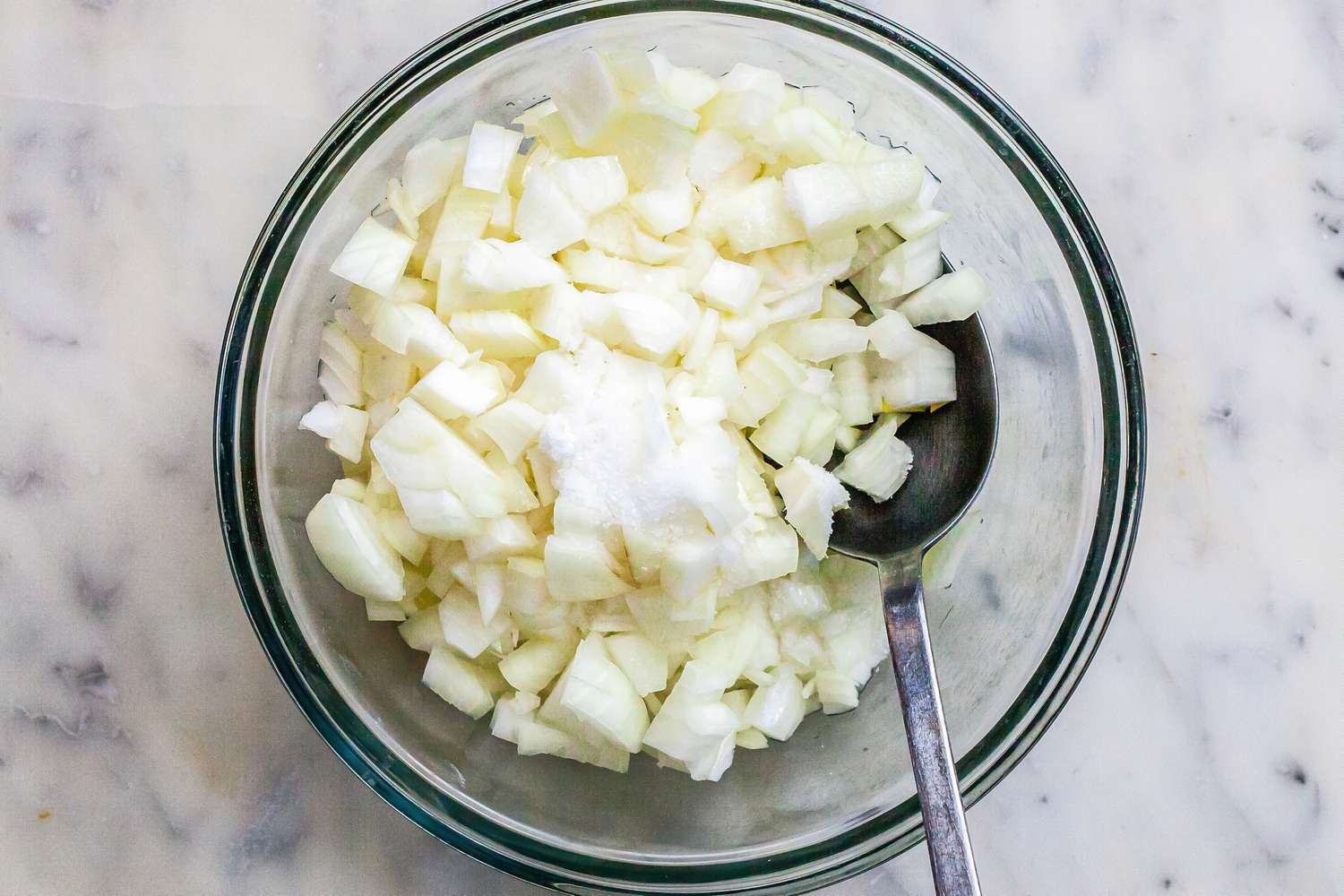 Chopped onions in a glass bowl with a spoon.