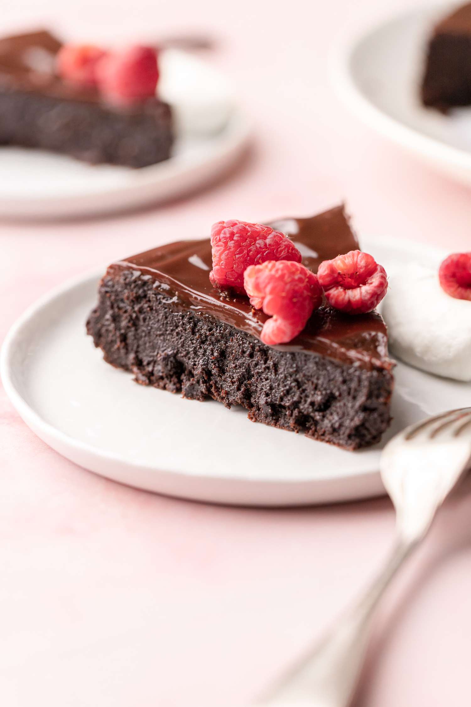 A Slice of Flourless Chocolate Cake Served on a Small Plate with Fresh Raspberries and Whipped Cream