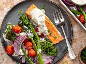 Overhead view of a gray plate of salmon, broccolini cherry tomatoes, onions and feta sauce with a fork on a marble countertop