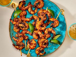 Platter of shrimp skewers with lime wedges, served on a blue plate accompanied by drinks