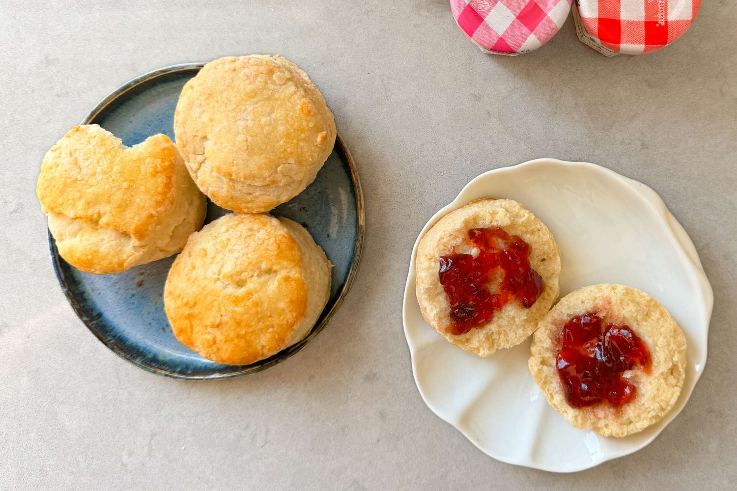 Two plates with British scones, one scone split in half with jam spread on both sides