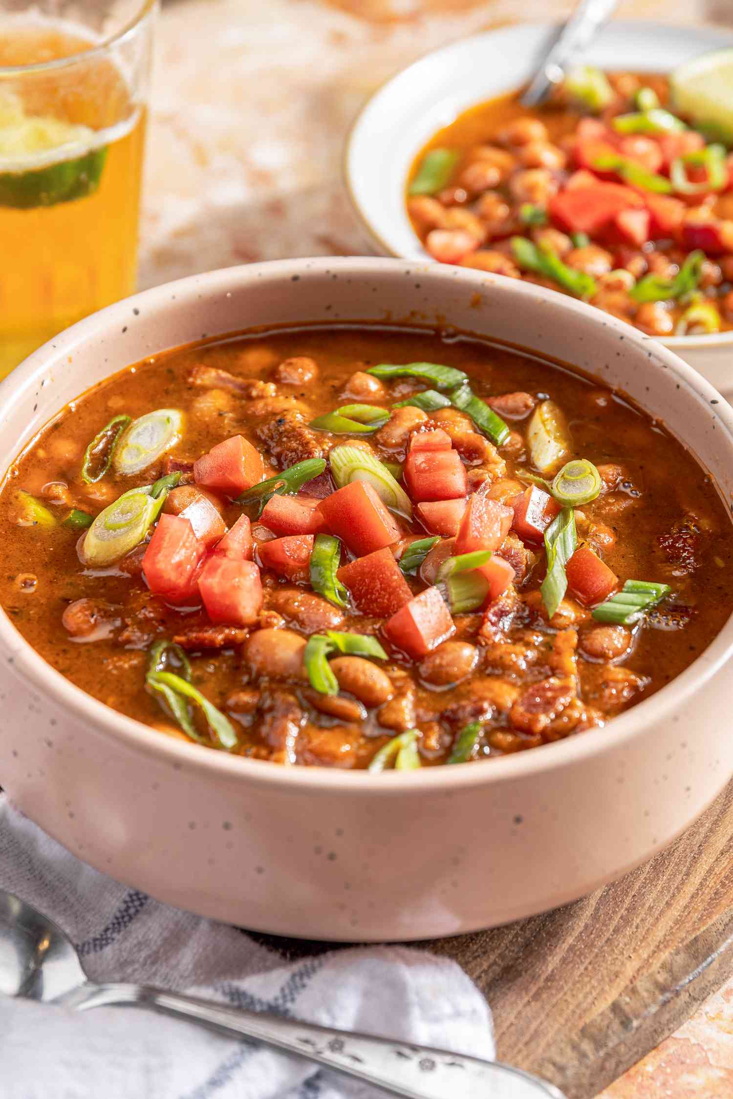 borracho beans (frijoles beans) in a bowl at a table setting, and in the background, a glass of beer and another serving