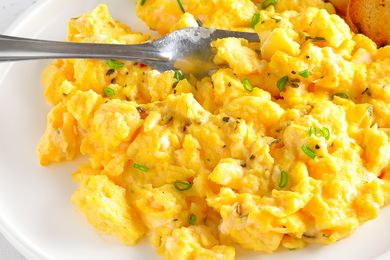 A close up of scrambled eggs on a white plate, garnished with chopped scallion