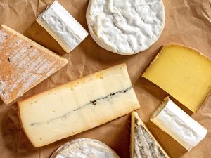 Various types of cheese arranged on brown parchment paper including soft and hard cheese varieties in multiple shapes and textures