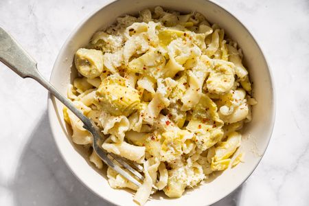 Bowl of pasta with artichoke hearts and lemon shavings fork placed on the side