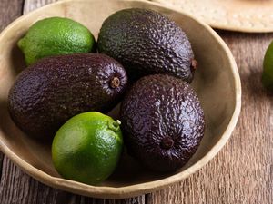 Bowl containing avocados and limes placed on a wooden surface