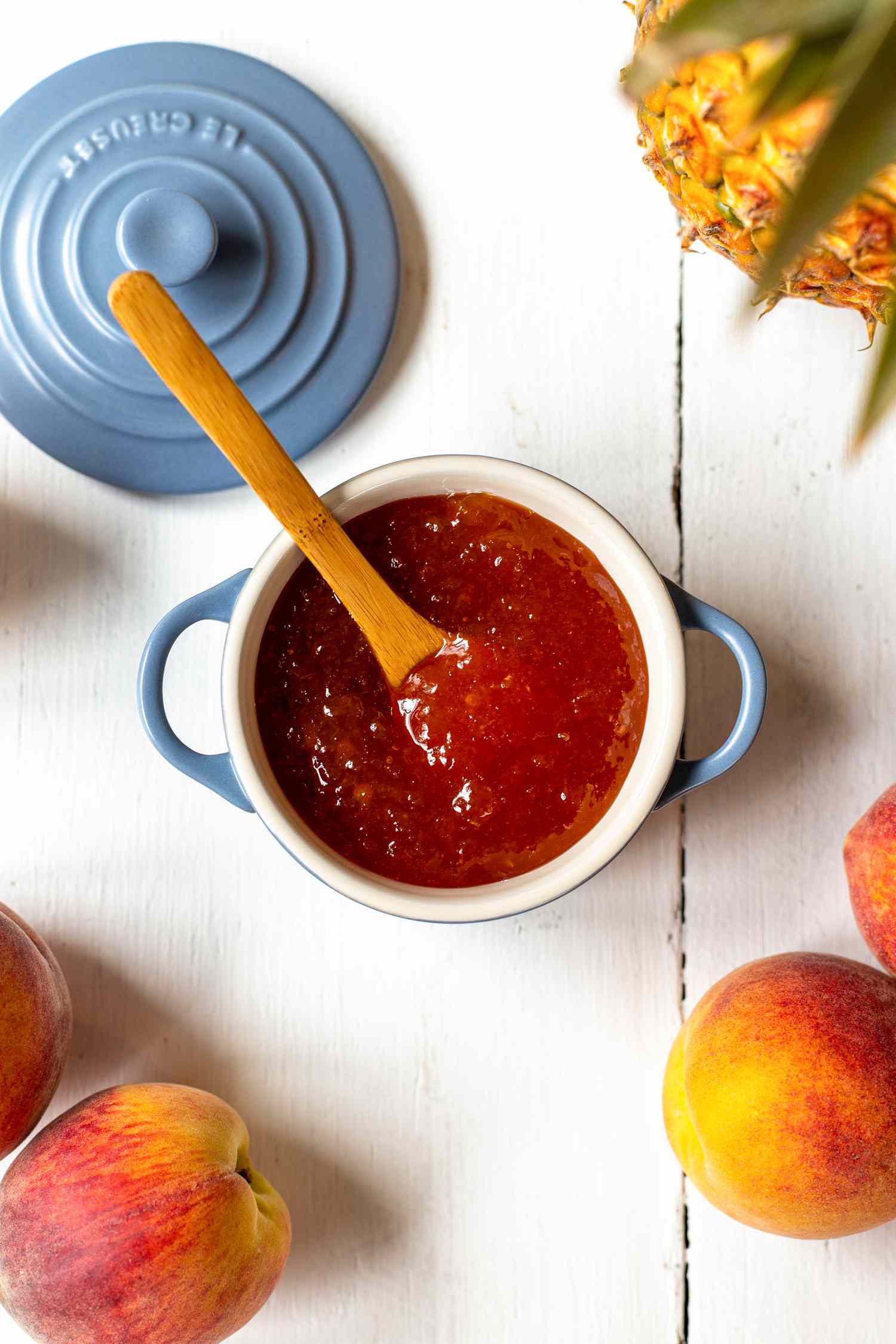 Peach and Pineapple Jam in a Small Dutch Oven Surrounded by Peaches and a Pineapple 