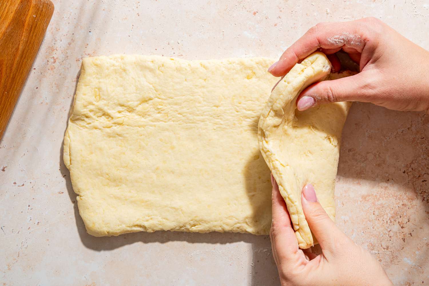 Overhead view of the dough rolled and two hands folding it over for the second time for Mayonnaise Biscuits recipe