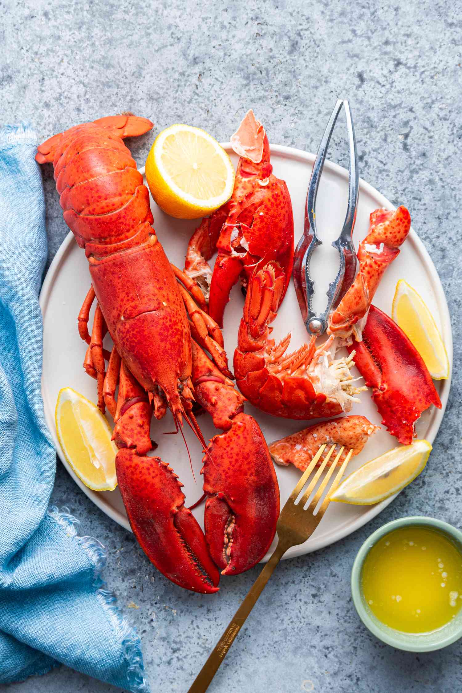 A cracked open lobster on a plate with a whole lobster next to it