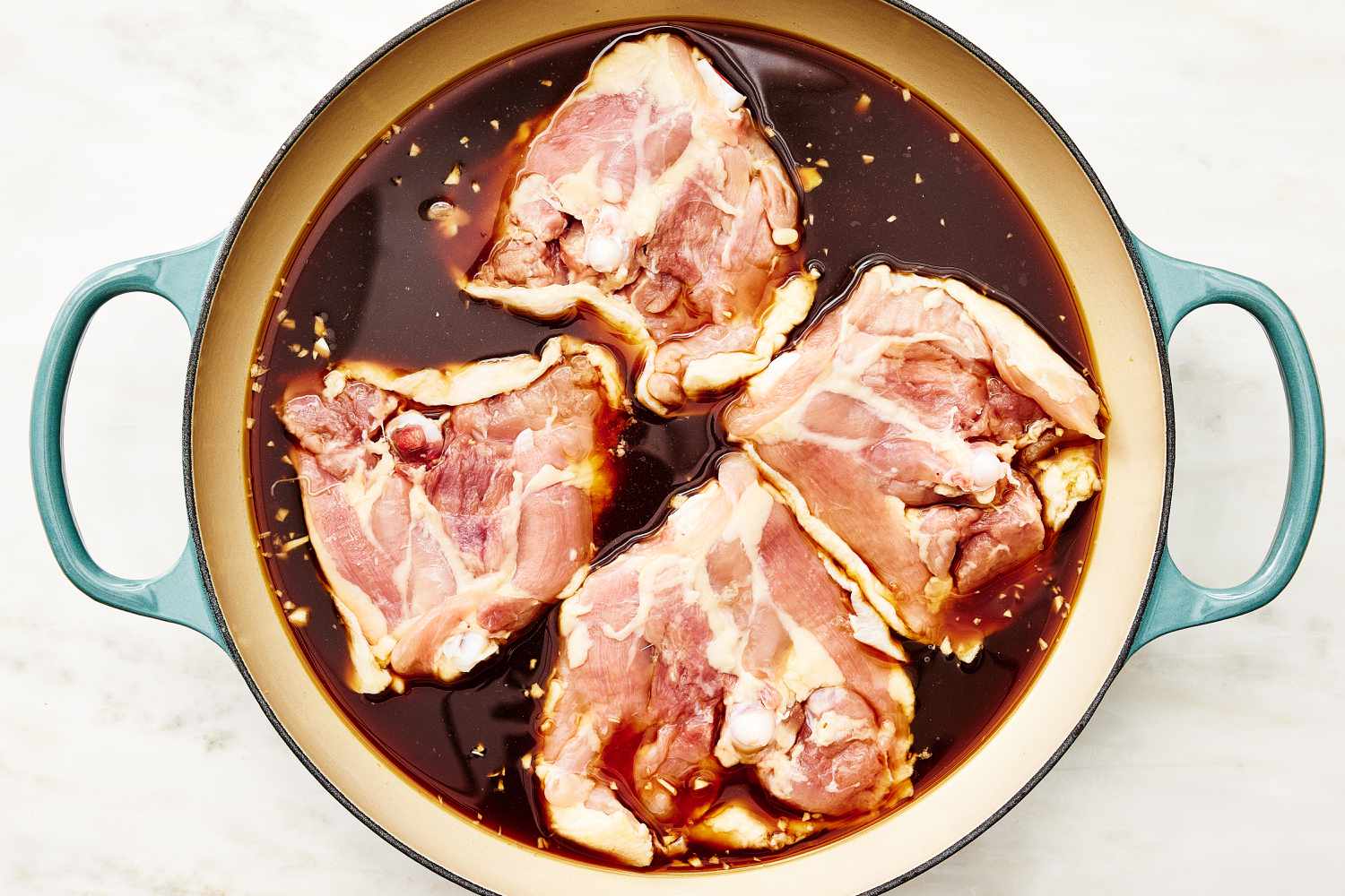 Overhead view of a large pot of four raw chicken thighs in soy sauce mixture for Shoyu Chicken recipe
