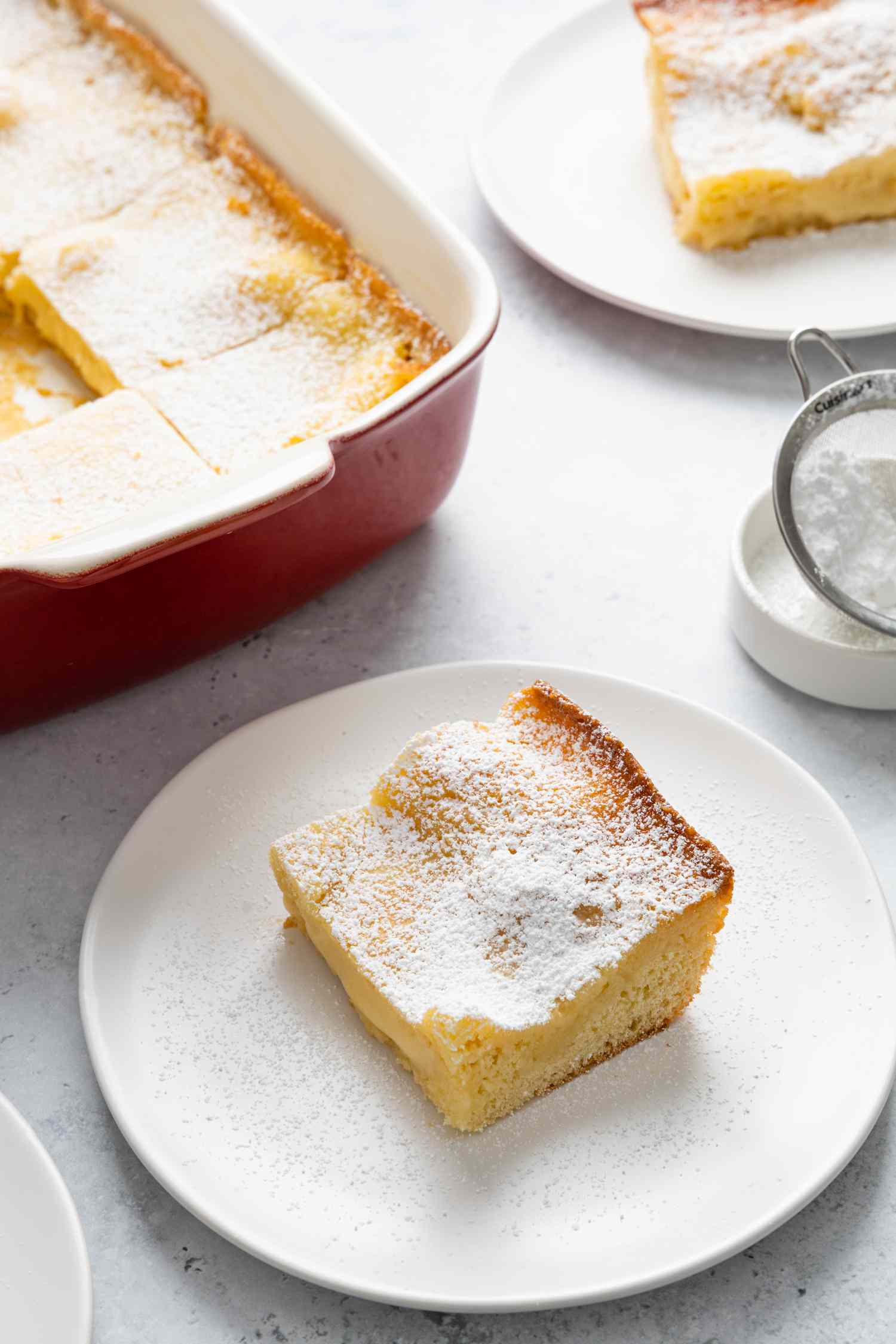 Gooey Butter Cake Slice on a Plate Next to a Baking Pan with More Cake