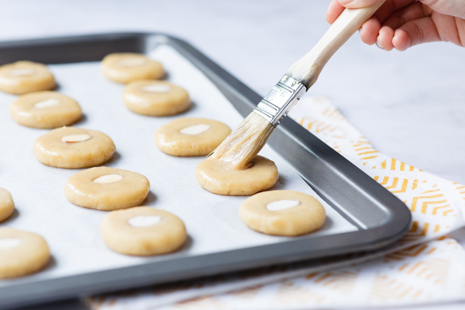 Brushing the almond topped cookies with a pastry brush.