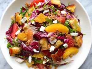 Horizontal overhead view of citrus salad on a white plate. Supremed orange and grapefruit, radicchio, croutons and feta cheese crumbles are visible.