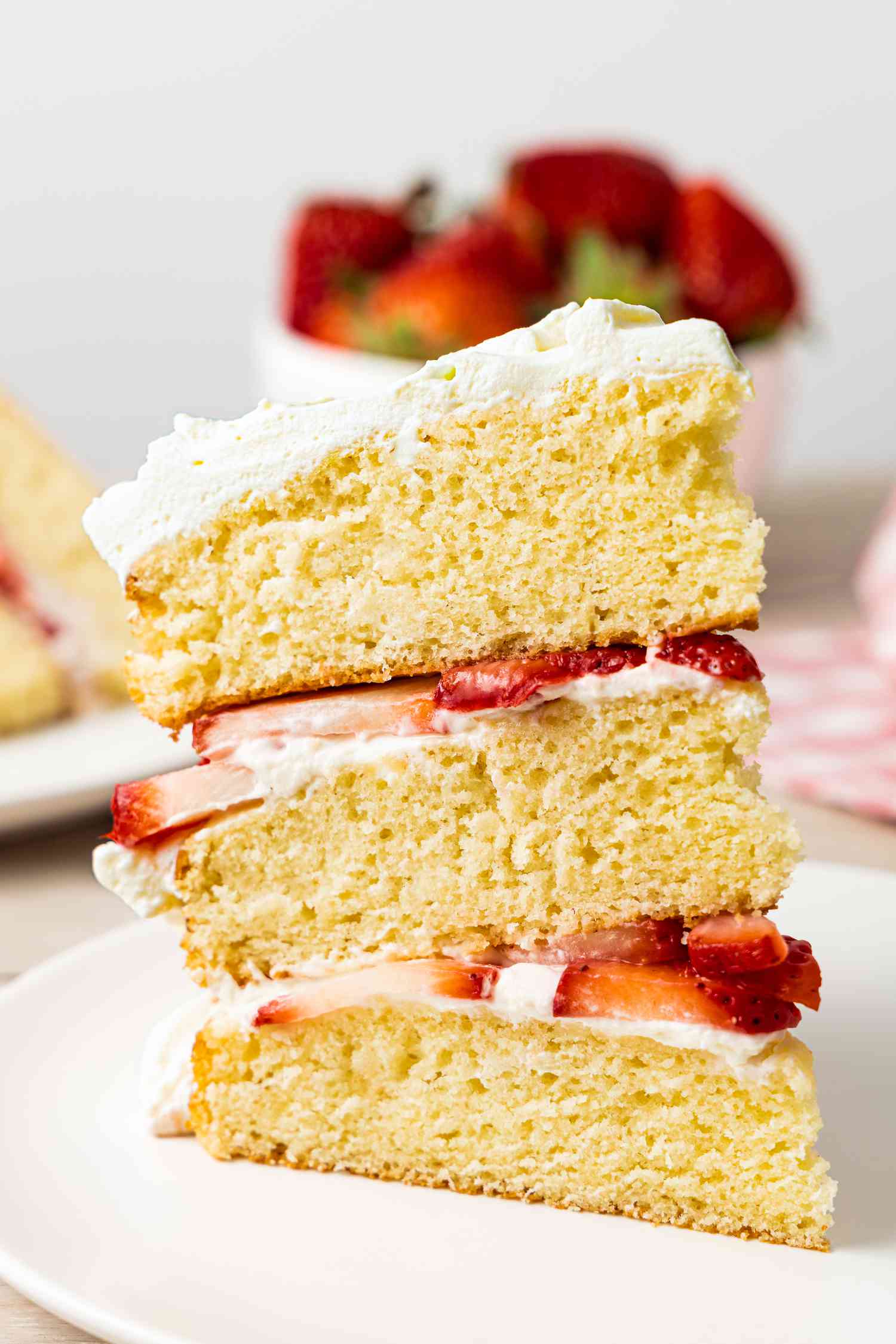 Slice of Strawberry Shortcake Cake on a Plate, and in the Background, a Bowl of Whole Strawberries