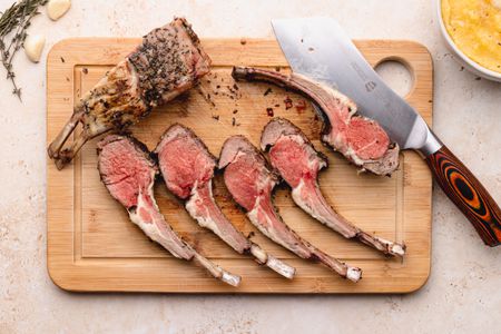 Rack of lamb cut into chops on cutting board with a knife