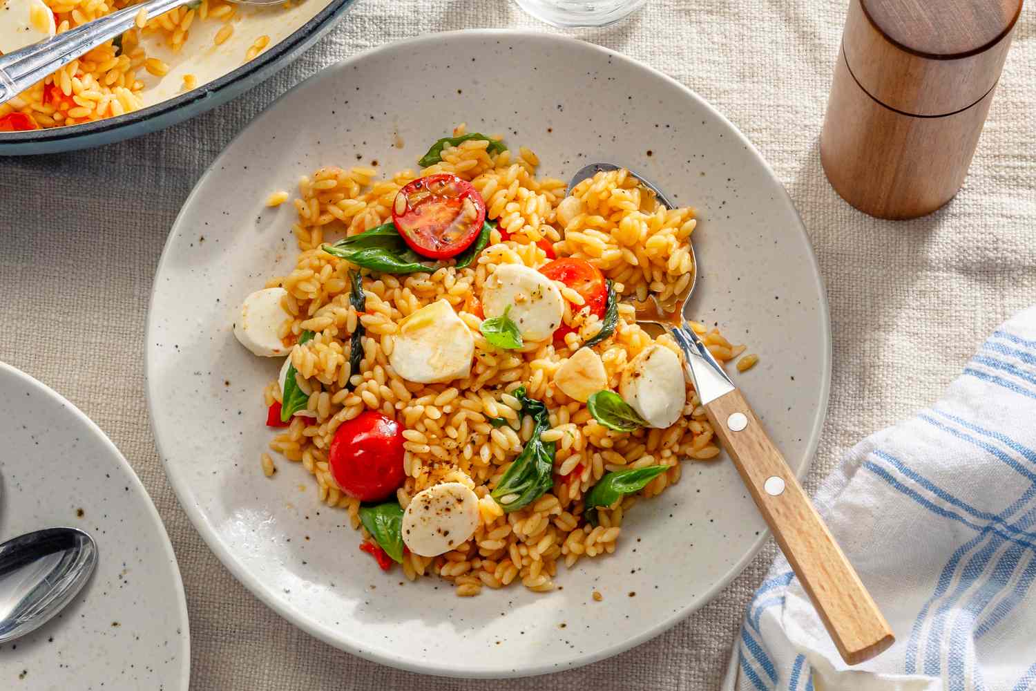 A plate of orzo pasta with cherry tomatoes mozzarella and fresh basil served with a fork