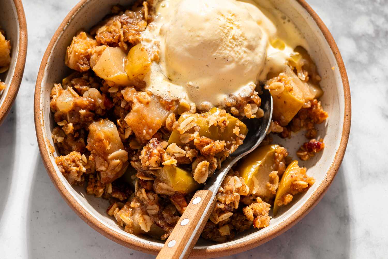 A bowl of apple crisp topped with ice cream and a spoon resting inside