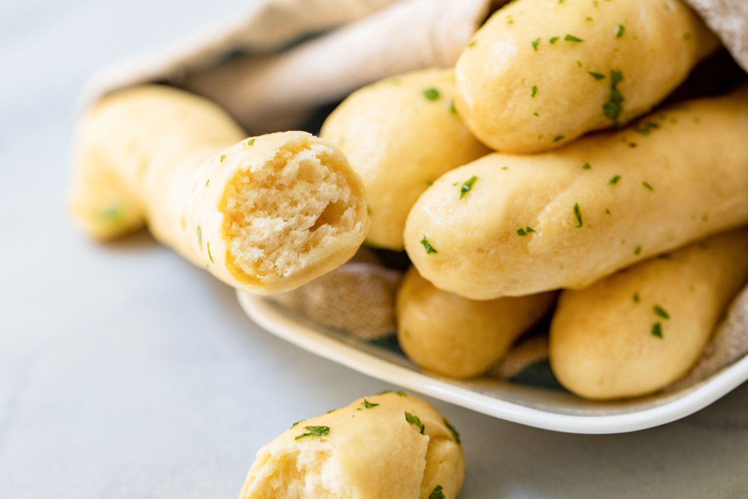 Breadsticks with Garlic Butter on a Plate Covered with a Kitchen Towel (One Breadstick Cut in Half)