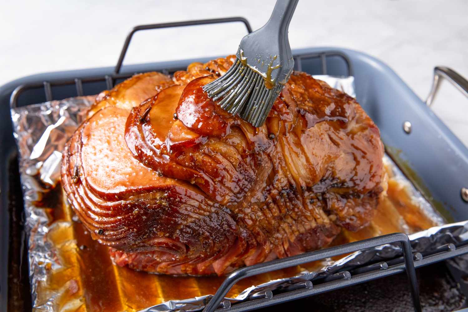 A glazed spiral ham being brushed with glaze in a roasting pan