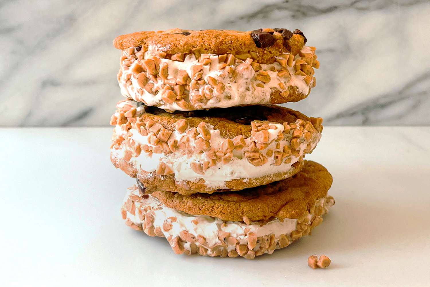 Three stacked ice cream sandwiches with cookie ends and toppings on a white surface