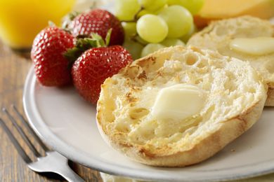 Close-up of an English muffin with melting butter; strawberries and grapes are on the same plate