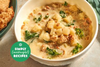 A bowl of soup with diced potatoes sausage and kale on a table setting with bread