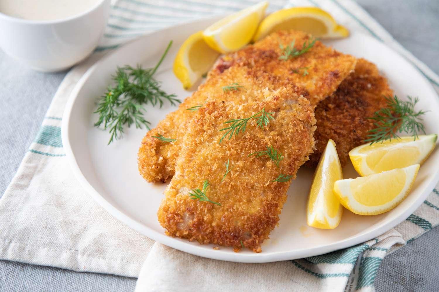 A plate of pork schnitzel on a white plate served with lemons and dill.