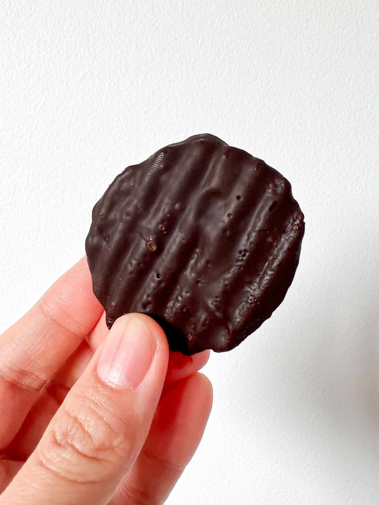 Hand holding a potato chip covered with chocolate