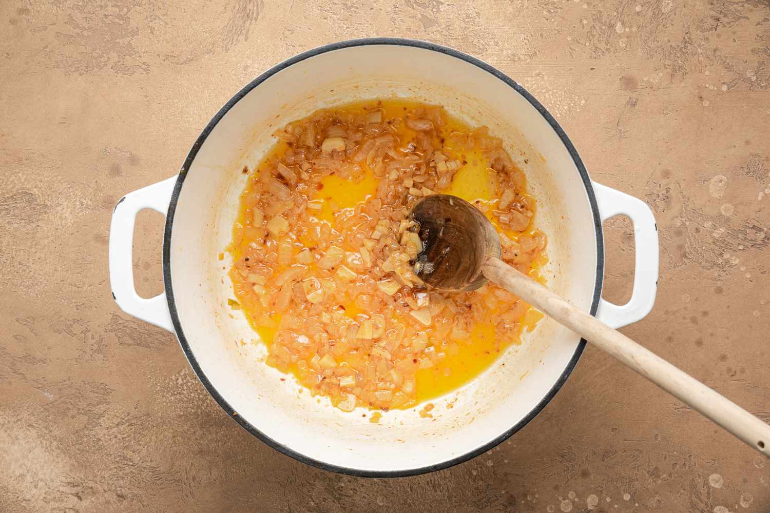 Cooked Aromatics in a Dutch Oven with a Spoon for Creamy White Bean Soup Recipe