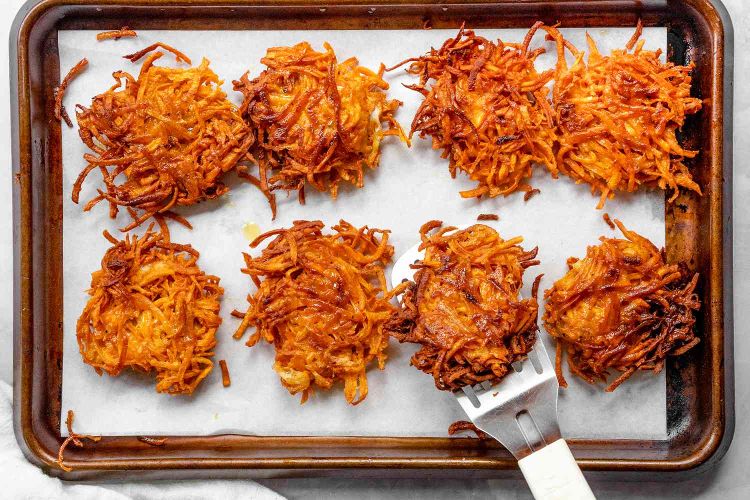 Sweet Potato Latkes on a Parchment Lined Baking Sheet with One on a Spatula