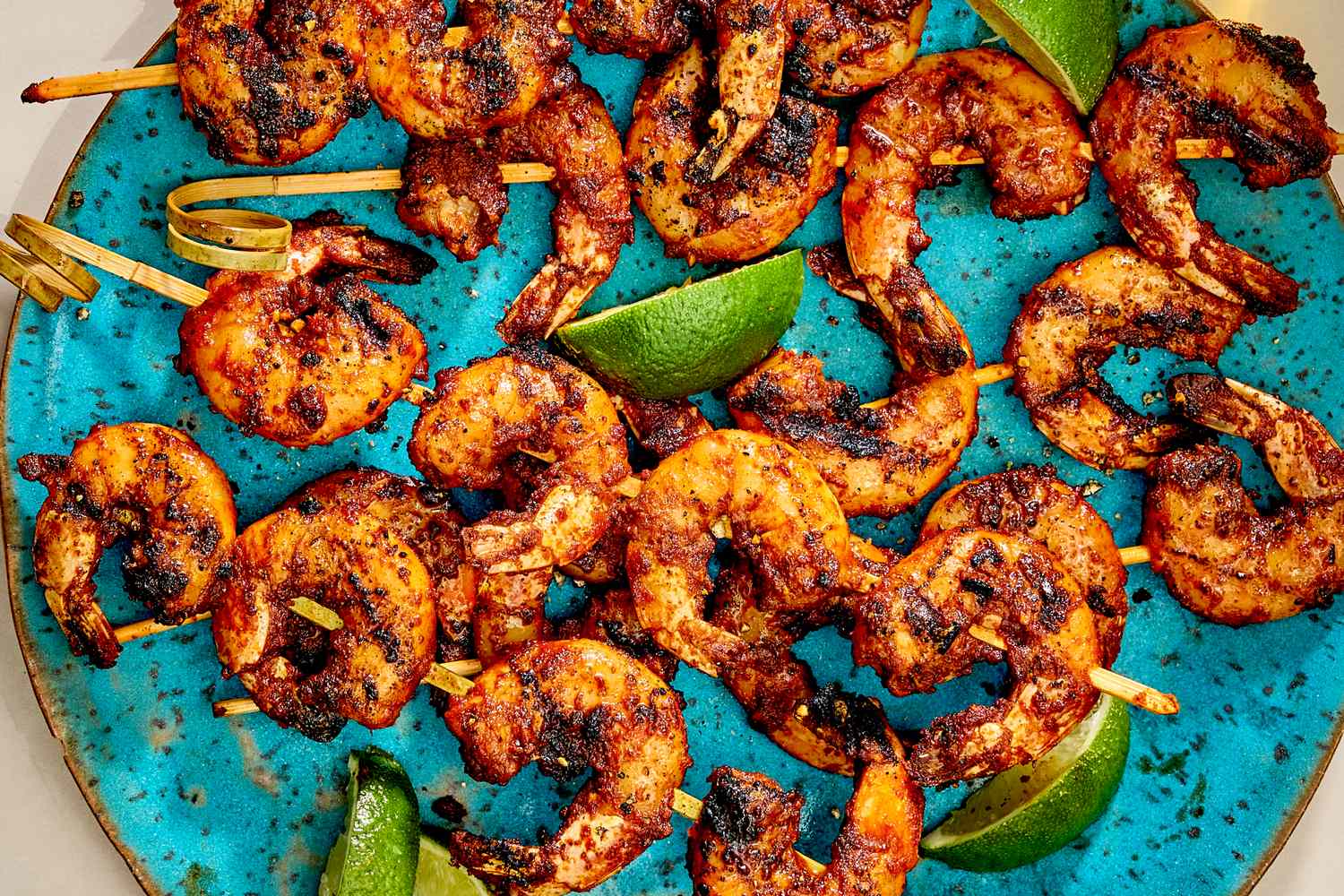 Grilled shrimp skewers arranged on a blue plate with lime slices