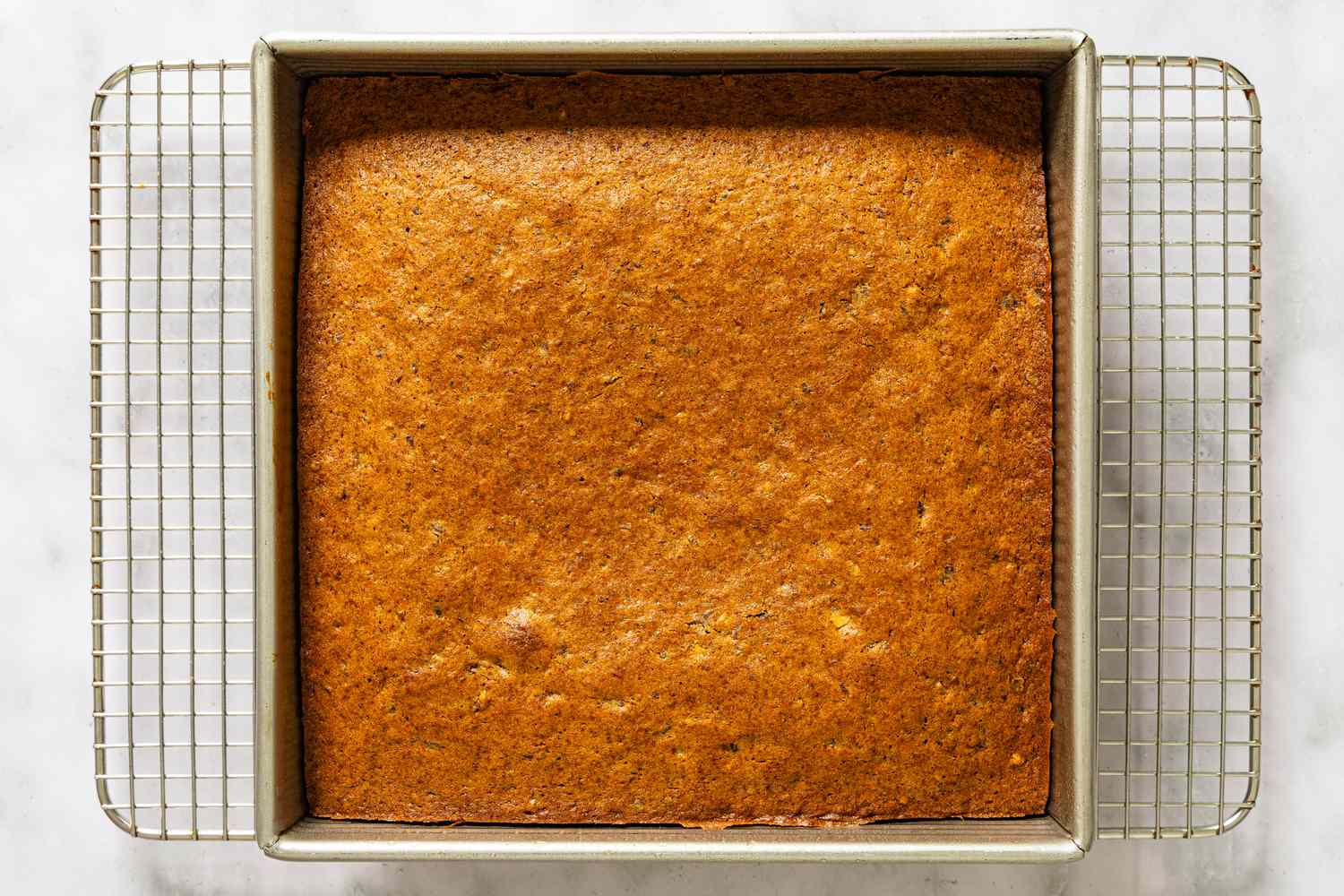 A baked cake in a square pan on a cooling rack