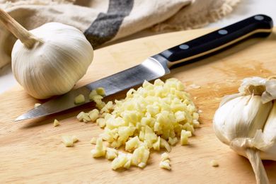 A cutting board with minced garlic a knife and whole garlic bulbs