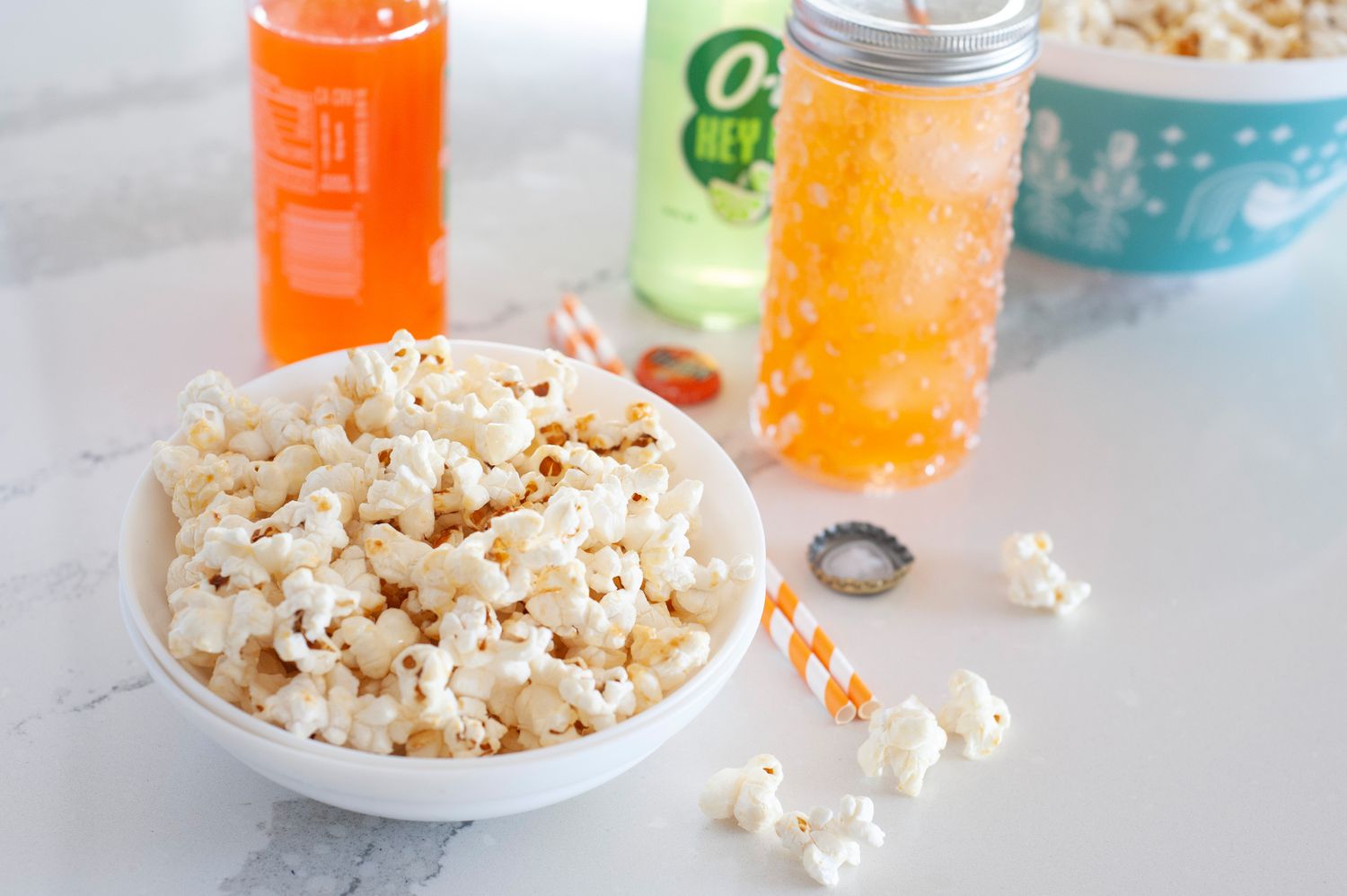 A bow of kettle popcorn set in front of orange sodas.