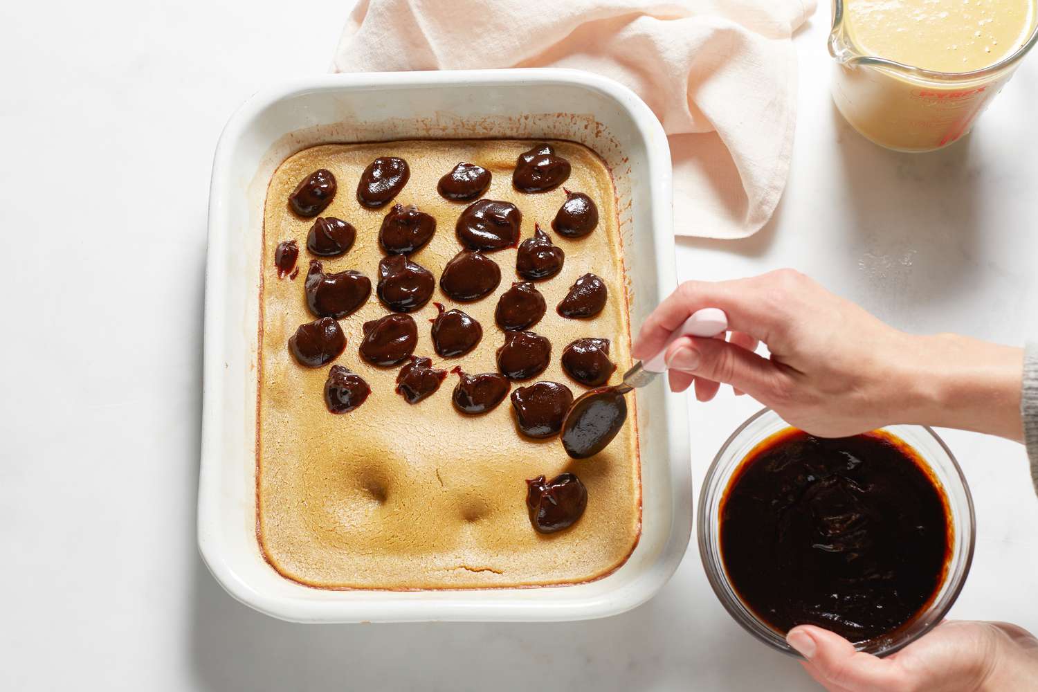 Pouring batter and spreading bean paste on a Sticky rice cake with red bean paste in a baking dish.