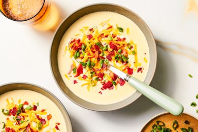 A bowl of loaded potato soup garnished with shredded cheese bacon bits and green onions with a spoon placed inside