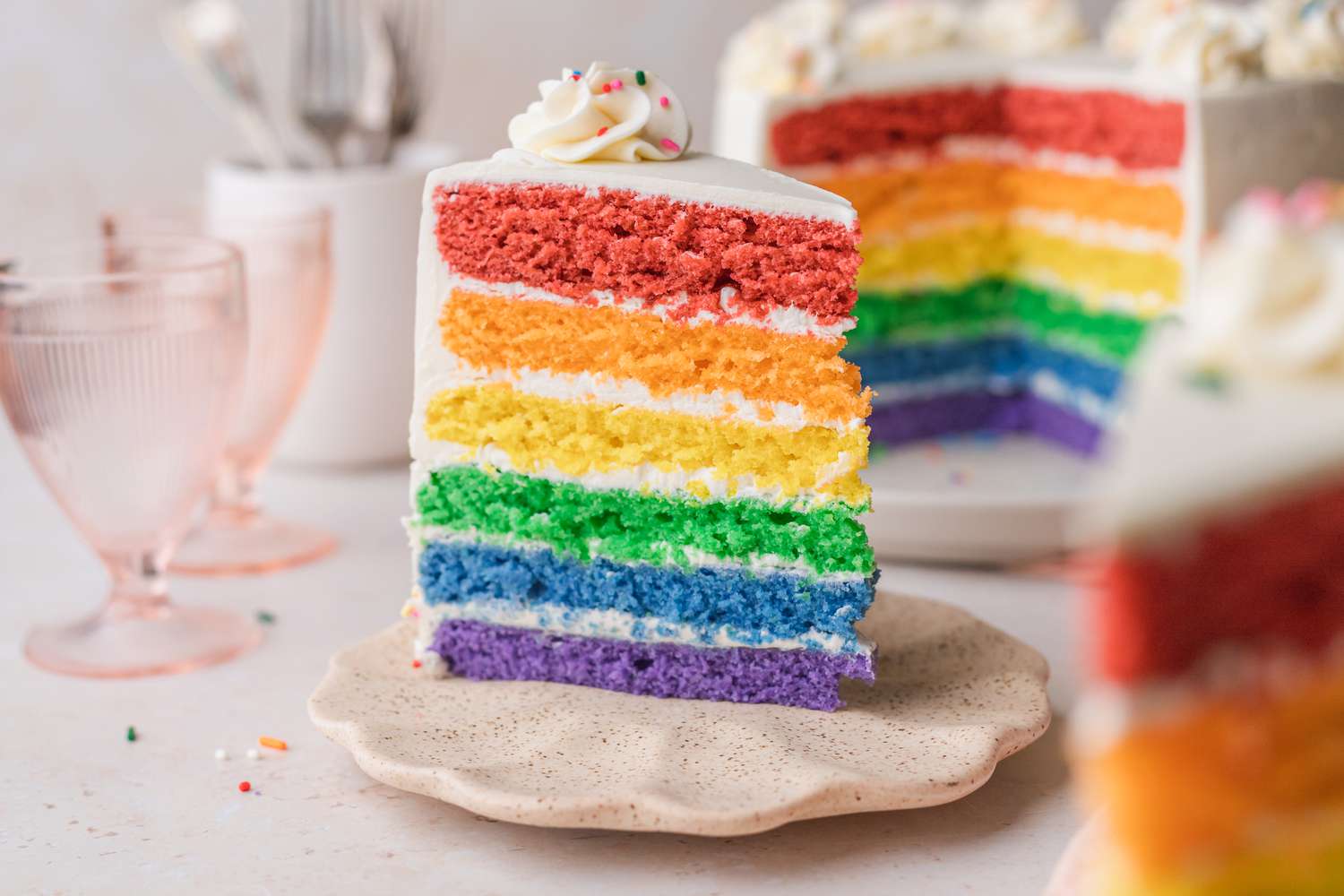 A Portion of Cake with Rainbow Layers Served on a Plate Surrounded by More Cake and Cups