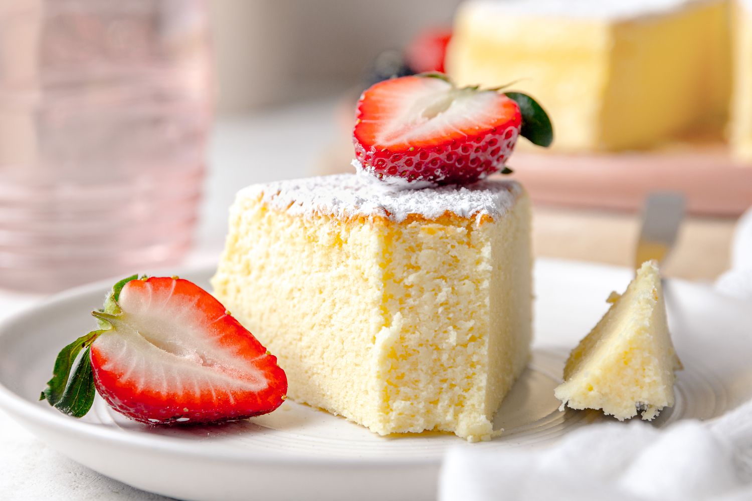 On a Small Plate, a Slice of Japanese Cheesecake With a Bite Size on the Fork Next to It, Served With Halved Strawberries