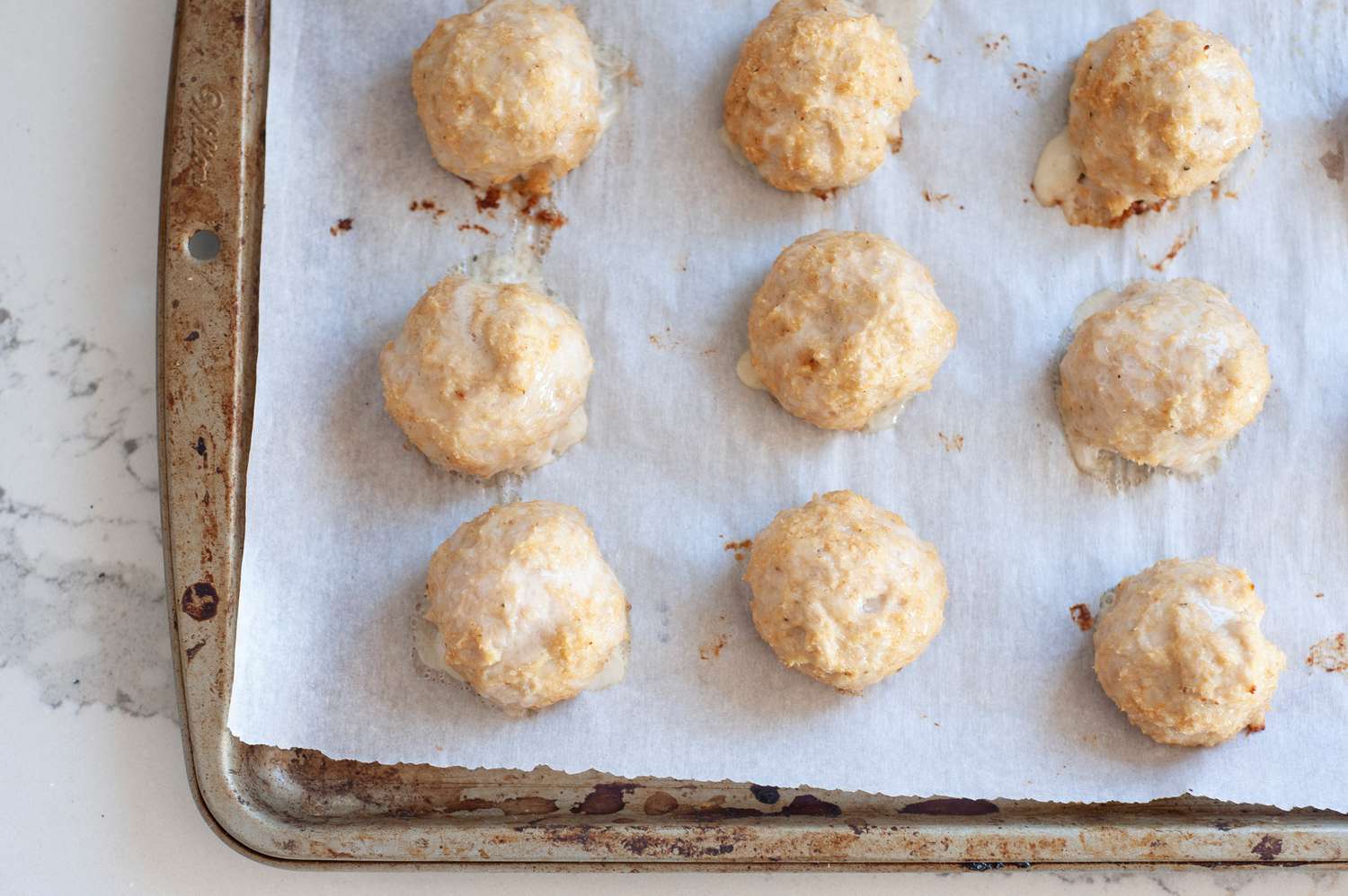 Baked chicken meatballs on baking sheet.