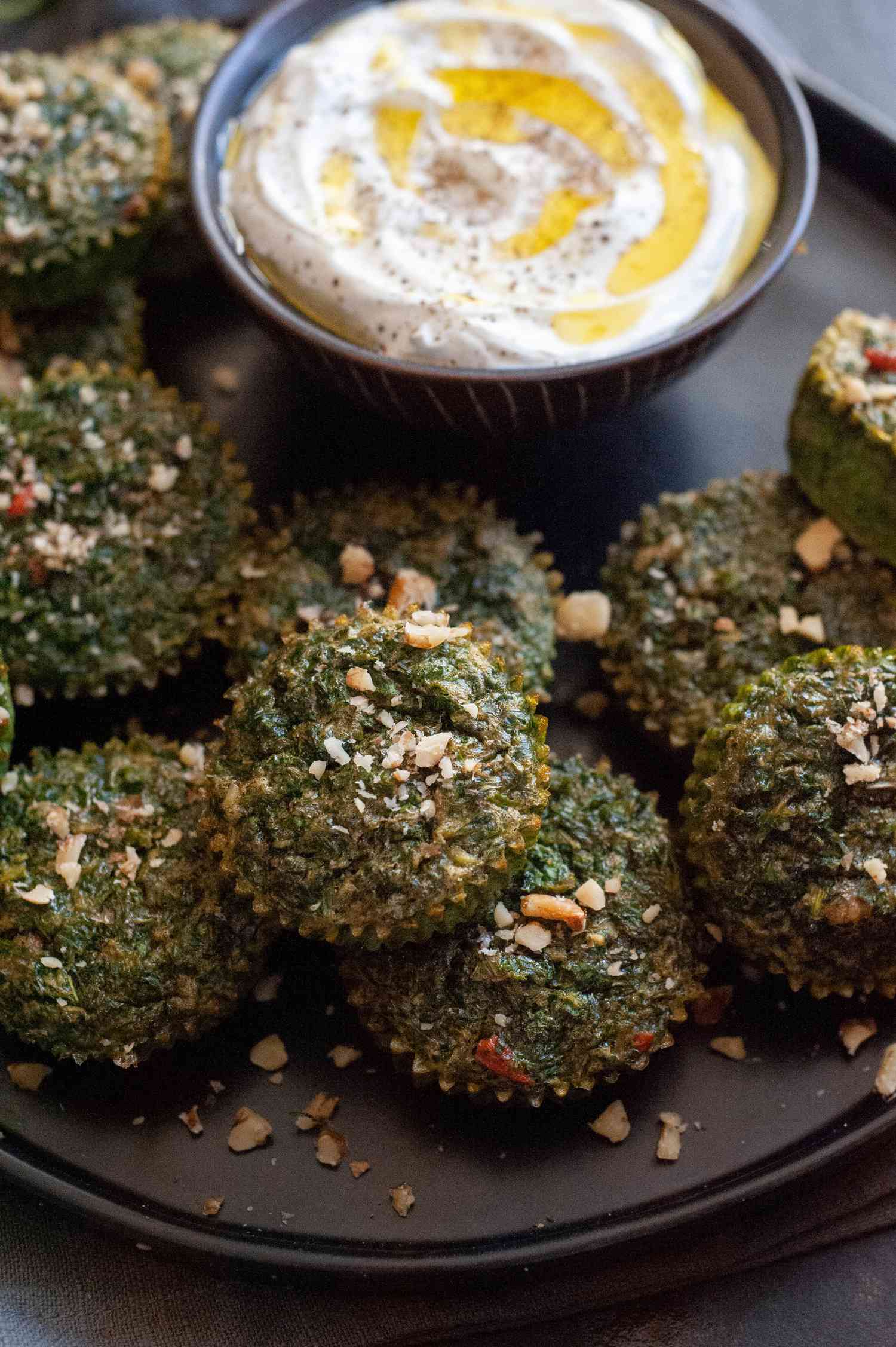 Kuku Sabzi on a black plate with yogurt dip on the side. 