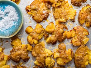 Crash hot potatoes and a small saucer with flaky salt on a baking sheet