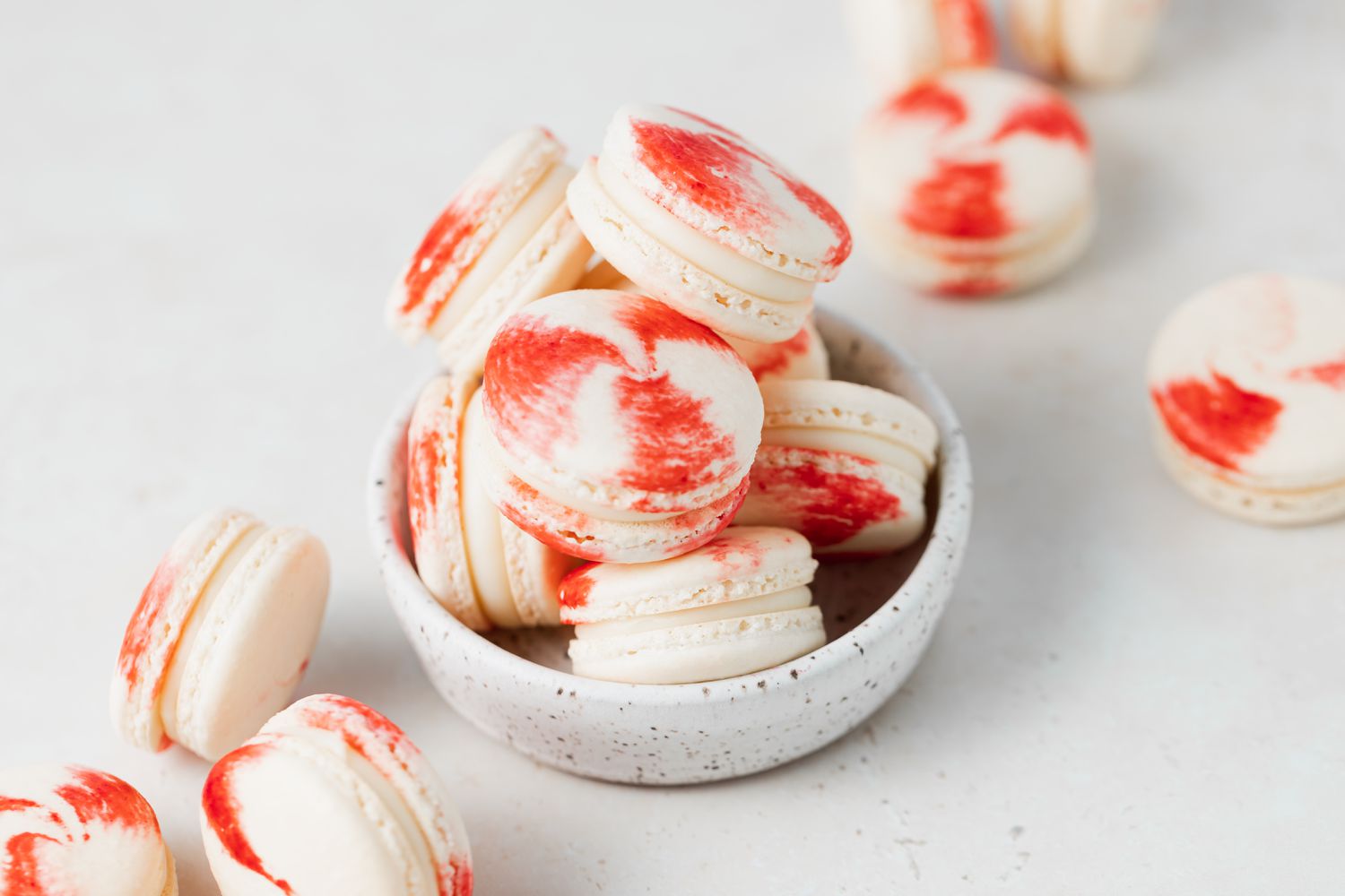 Macarons with peppermint and white chocolate filling stacked in a bowl with more set around it.
